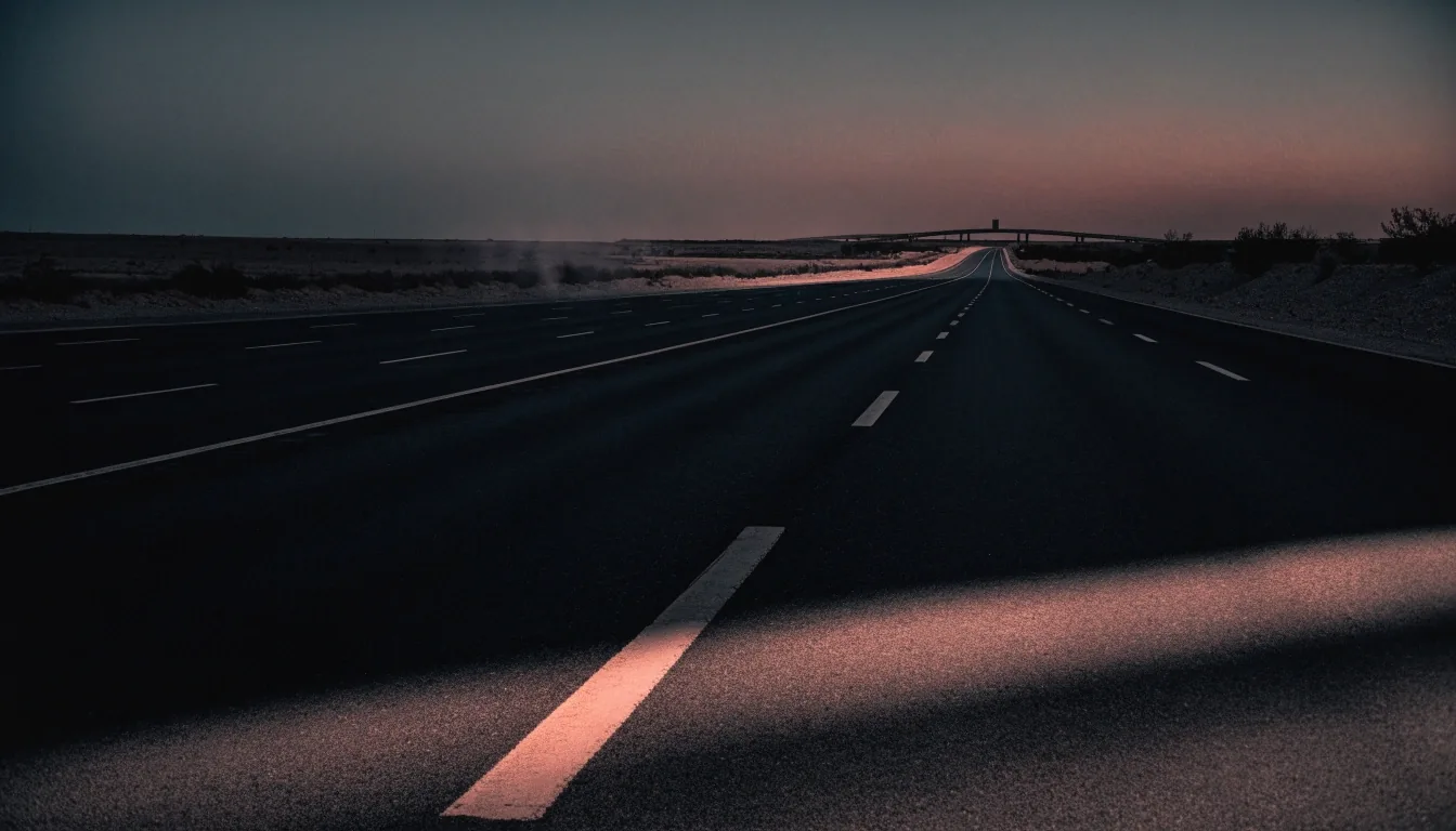 Empty multi-lane desert highway at dusk with lane markings receding toward a distant interchange